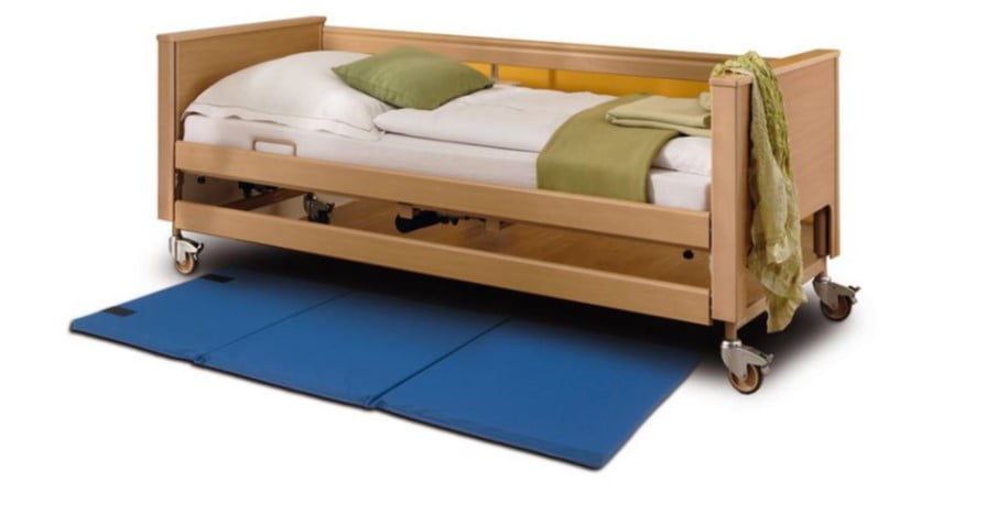 Blauwe opvouwbare valpreventiemat Aidapt naast een houten zorgbed om letsel bij vallen uit bed te beperken.