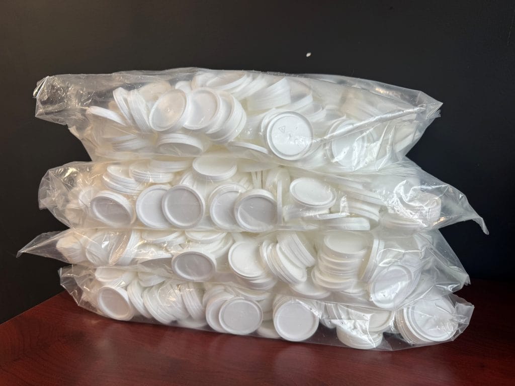 Tweedekans: Severo deksels voor cups voor medicijnvermaler, schuin aanzicht van volle zak witte deksels op houten tafel.