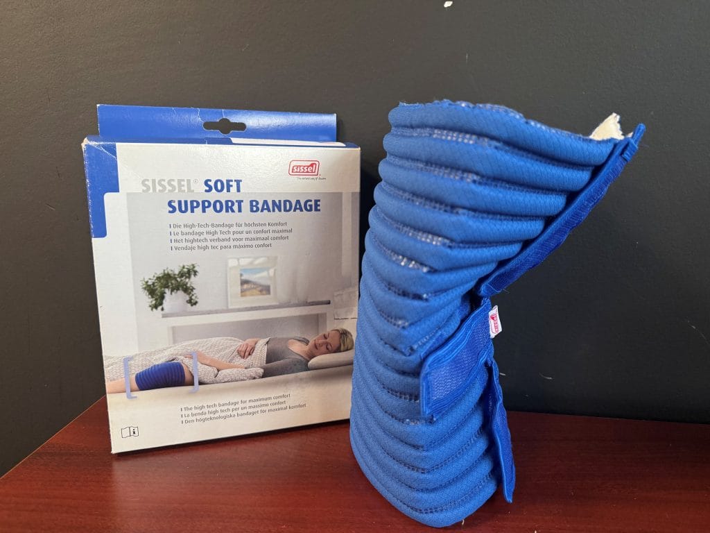 Tweedekans Sissel knie bandage, blauwe zachte steunbandage op tafel met productverpakking erachter.